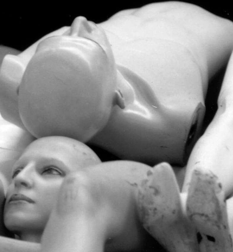 Manichini da vetrina ammucchiati e smembrati, fotografati in bianco e nero: teste e arti separati dai corpi.