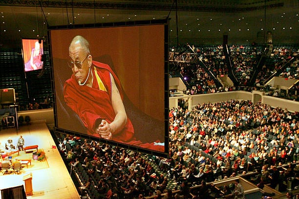 Il Dalai Lama sul maxischermo di un auditorium gremito di pubblico